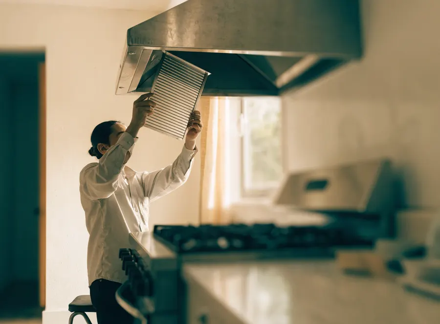 Técnico retirando el filtro metálico de una campana extractora de cocina.
